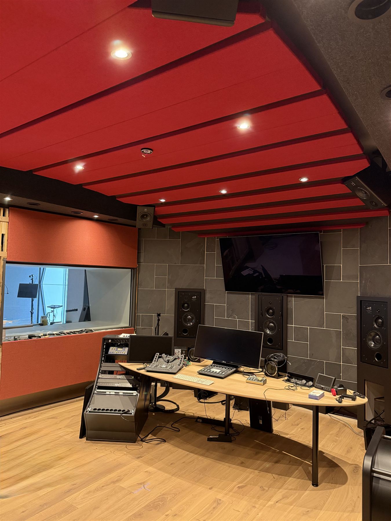 Dolby Atmos mixing suite with red acoustic ceiling baffles, ATC monitors and kidney mixing desk
