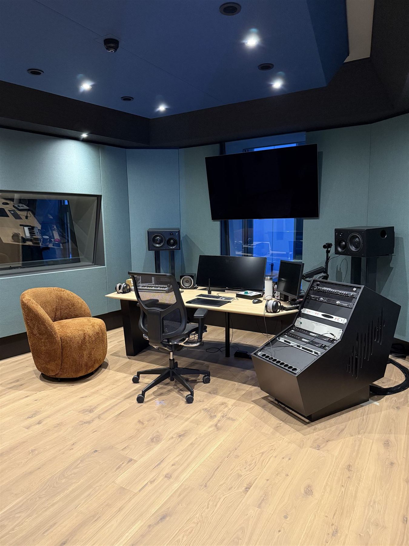 Producer control room in teal and blue, with cognac bouclé chair, oak floor and ATC monitors