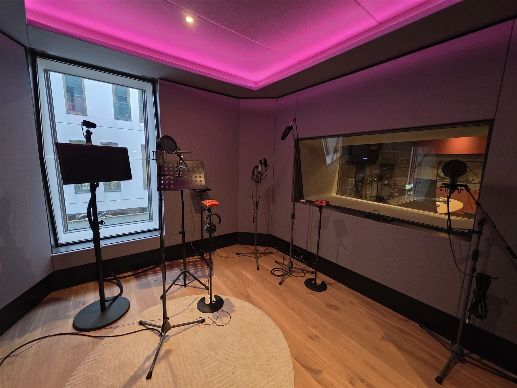Vocal recording booth in pink with LED cove lighting, sightline window to control room